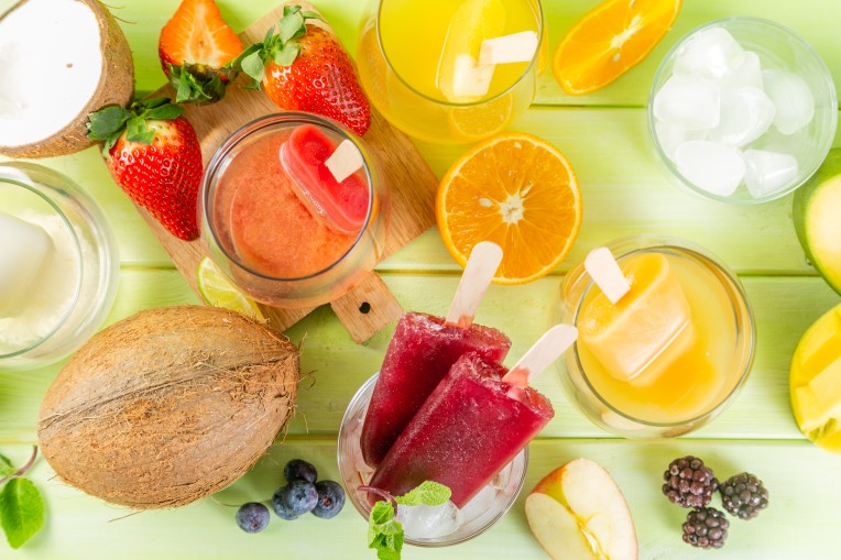 Selection of colourful ice pops and ingredients on green wood background, copy space